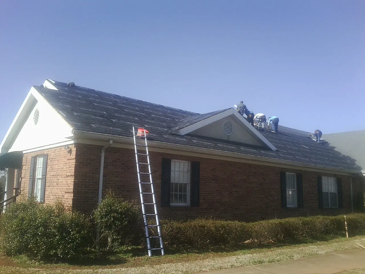 Crew tearing shingles off a brick ranch roof with a ladder set — Metal Roof Repair work by our crew in Pomfret