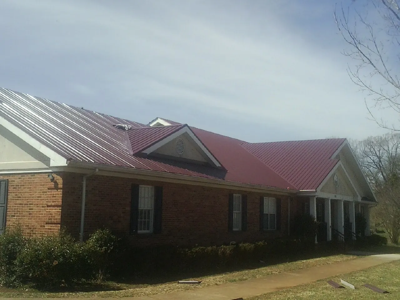 Red metal roof with gabled entries on a long brick building, from a Hail Damage Roof Repair job in Pomfret