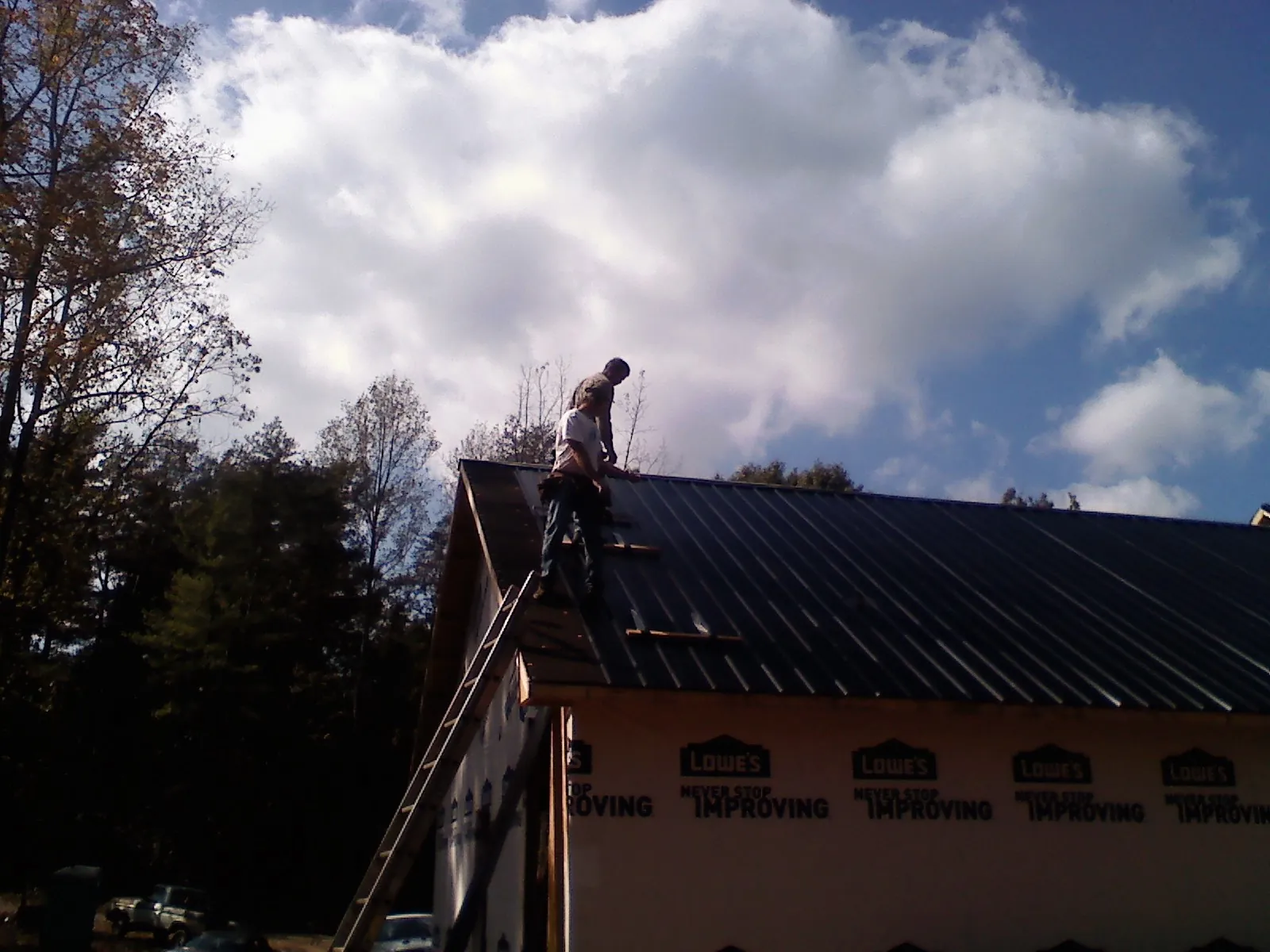 Roofer fastening dark metal panels high against a cloudy sky, from a Roof Inspection job in Pomfret