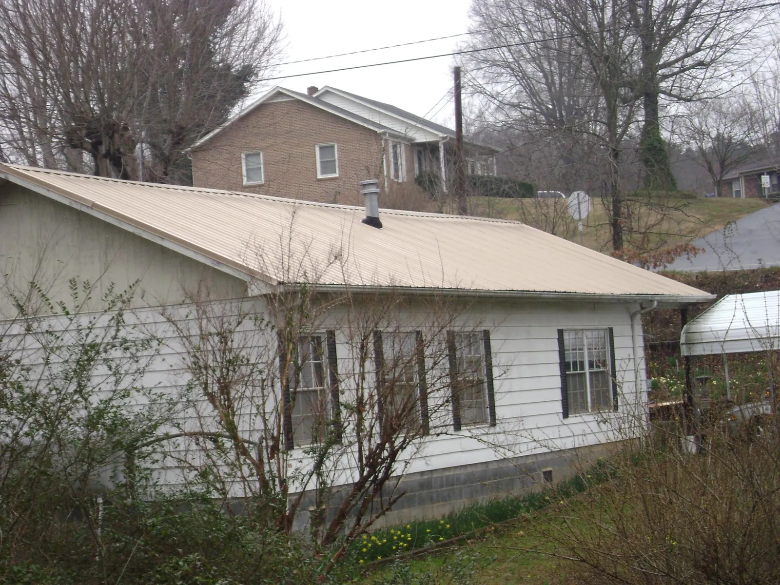 Tan metal roof on a white sided house set into a hillside — Commercial Roofing by Roofing Brothers in Pomfret